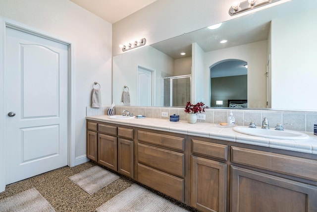 full bathroom with double vanity, a stall shower, backsplash, and a sink