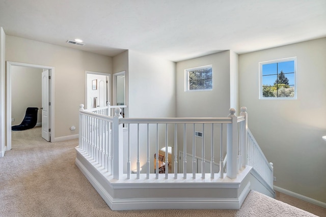 hallway featuring an upstairs landing, carpet flooring, visible vents, and baseboards