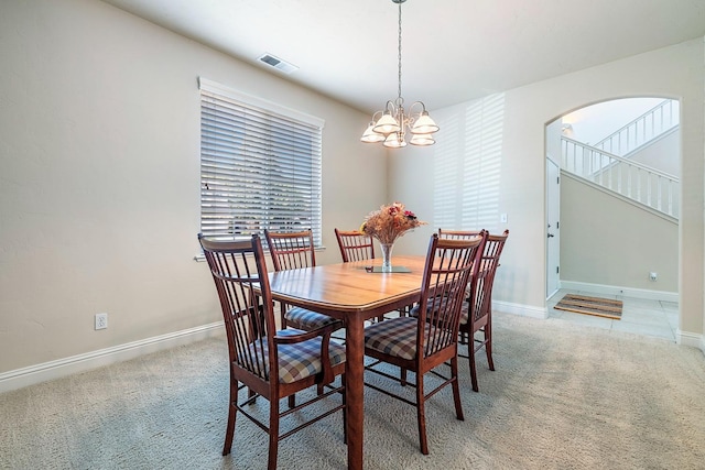 dining space featuring light carpet, arched walkways, a chandelier, and baseboards