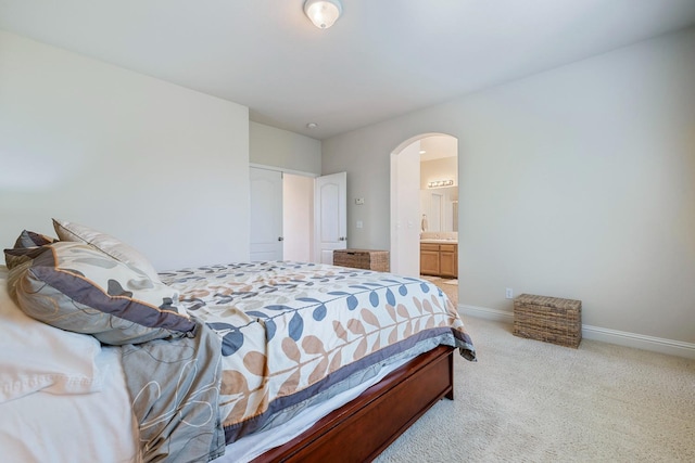 carpeted bedroom featuring baseboards, arched walkways, and ensuite bathroom