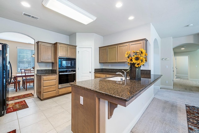 kitchen featuring visible vents, arched walkways, dark stone countertops, black appliances, and a sink