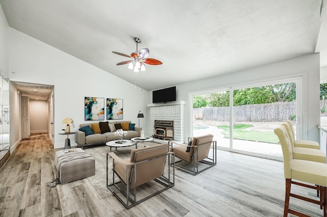 living room featuring a ceiling fan, lofted ceiling, wood finished floors, a textured ceiling, and a brick fireplace