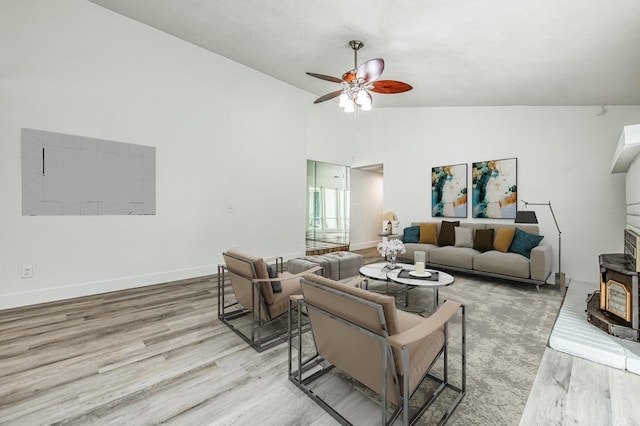 living area featuring baseboards, a wood stove, light wood-style flooring, and a ceiling fan