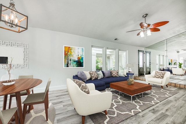 living area with light wood-type flooring, visible vents, baseboards, and ceiling fan with notable chandelier