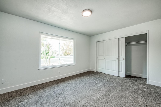 unfurnished bedroom featuring a closet, dark carpet, a textured ceiling, and baseboards