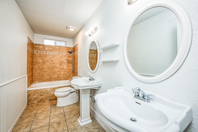 bathroom featuring a wainscoted wall, tiled shower / bath, toilet, a sink, and a textured ceiling