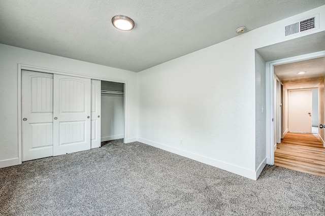 unfurnished bedroom featuring baseboards, visible vents, a textured ceiling, carpet flooring, and a closet