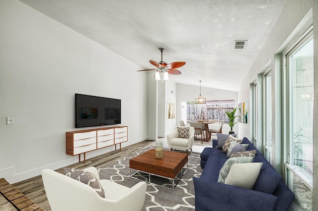 living area with lofted ceiling, a textured ceiling, wood finished floors, visible vents, and baseboards