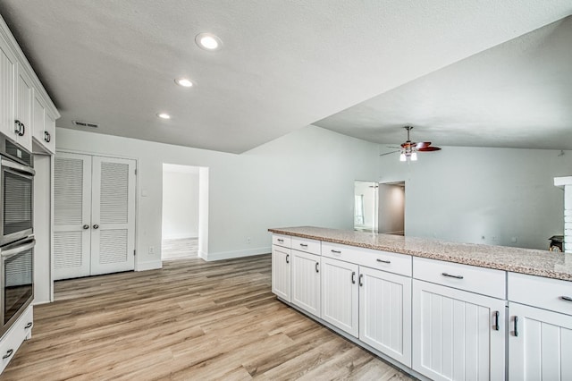 kitchen featuring visible vents, light wood-style flooring, vaulted ceiling, stainless steel double oven, and white cabinetry