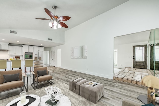 living area with high vaulted ceiling, light wood-style flooring, visible vents, baseboards, and a ceiling fan