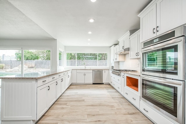 kitchen featuring white cabinetry, appliances with stainless steel finishes, light wood-type flooring, backsplash, and light stone countertops