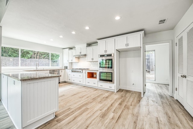 kitchen featuring light wood-style flooring, under cabinet range hood, stainless steel appliances, white cabinets, and light stone countertops