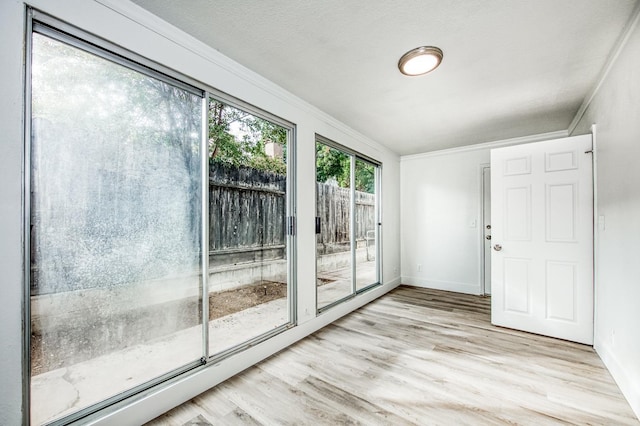 doorway featuring light wood-style flooring, a textured ceiling, baseboards, and crown molding