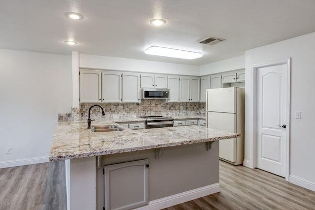 kitchen with stainless steel appliances, a peninsula, a sink, visible vents, and tasteful backsplash