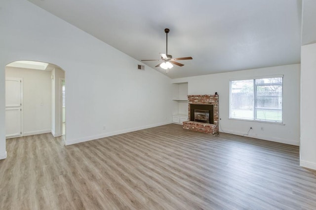 unfurnished living room featuring arched walkways, a ceiling fan, baseboards, light wood-type flooring, and a brick fireplace