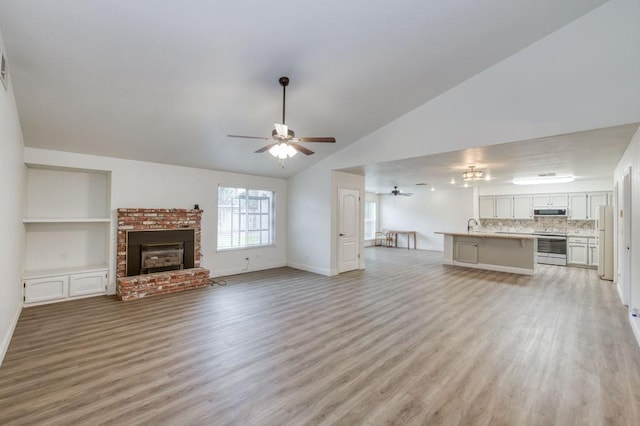 unfurnished living room with lofted ceiling, a fireplace, ceiling fan, and light wood finished floors