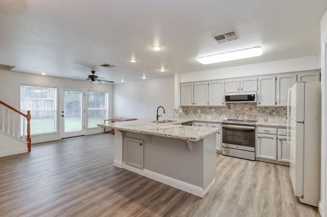 kitchen featuring a peninsula, stainless steel electric range oven, visible vents, and freestanding refrigerator