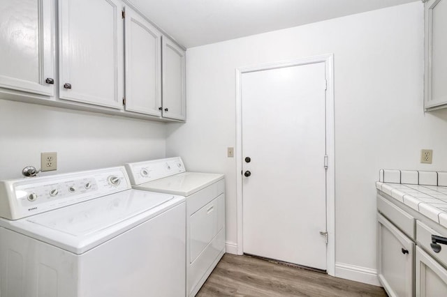 washroom featuring light wood finished floors, separate washer and dryer, cabinet space, and baseboards