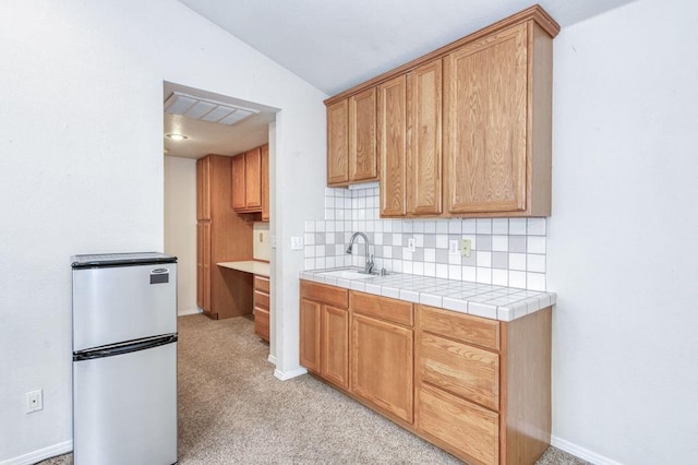 kitchen featuring tasteful backsplash, light colored carpet, lofted ceiling, freestanding refrigerator, and a sink