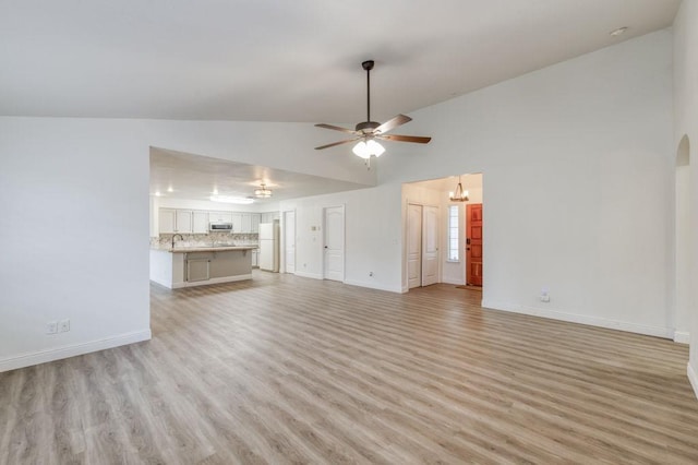 unfurnished living room featuring ceiling fan, arched walkways, light wood-style flooring, and baseboards