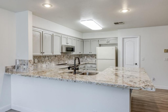 kitchen featuring tasteful backsplash, stainless steel microwave, freestanding refrigerator, a peninsula, and a sink