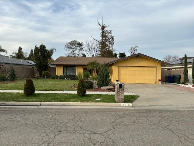 ranch-style home featuring an attached garage, driveway, a front yard, and stucco siding