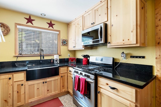 kitchen featuring dark countertops, light brown cabinets, appliances with stainless steel finishes, and a sink