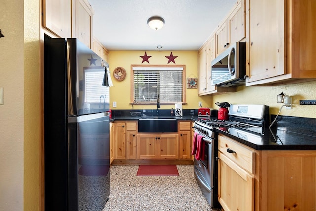 kitchen with light brown cabinets, stainless steel appliances, dark countertops, and a sink