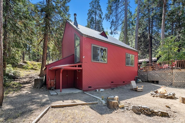 view of side of property featuring crawl space, a deck, a fire pit, and metal roof