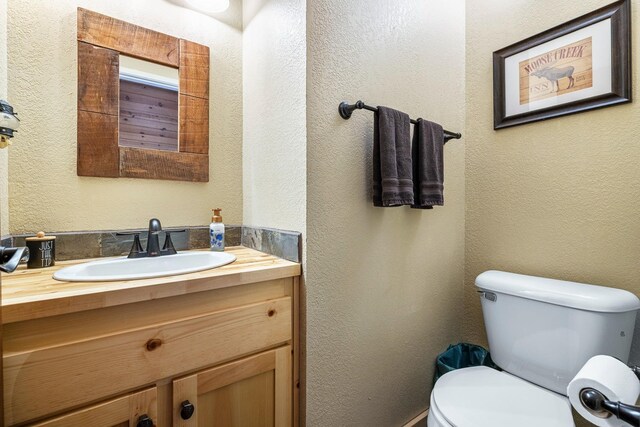 half bath featuring a textured wall, vanity, and toilet