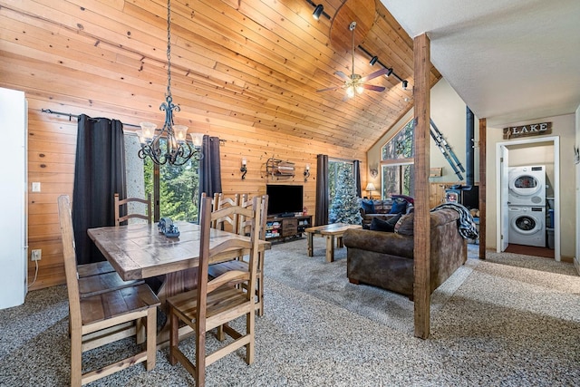 carpeted dining space with ceiling fan with notable chandelier, high vaulted ceiling, wood walls, and stacked washer and clothes dryer