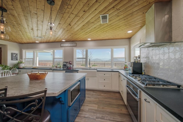 kitchen featuring a sink, visible vents, white cabinets, appliances with stainless steel finishes, and wall chimney exhaust hood