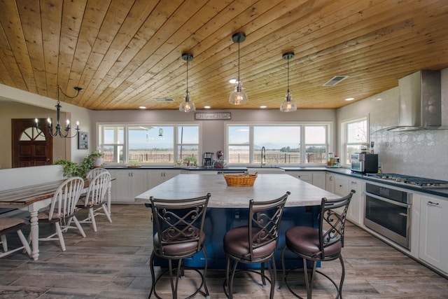 kitchen featuring dark wood-style floors, a center island, stainless steel appliances, backsplash, and wall chimney exhaust hood