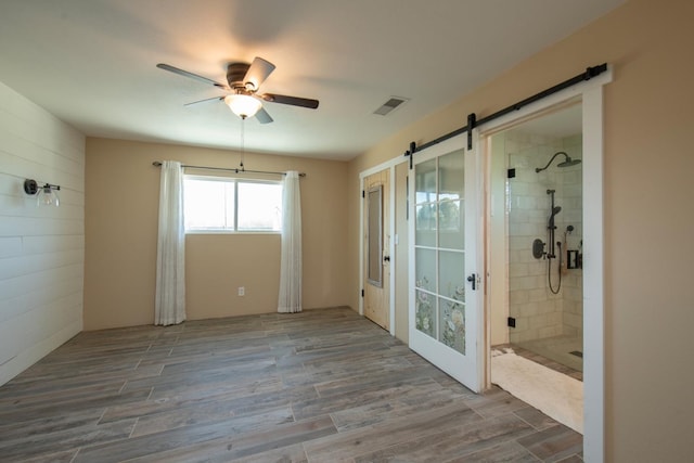 empty room featuring a ceiling fan, a barn door, visible vents, and wood finished floors