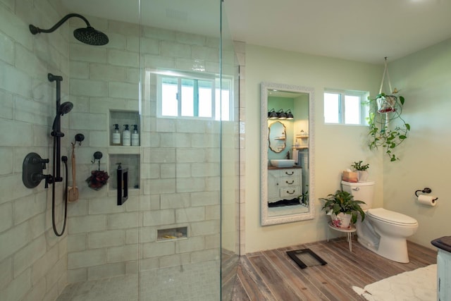 full bath featuring tiled shower, vanity, toilet, and wood finished floors