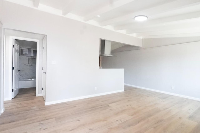 empty room with lofted ceiling with beams, light wood finished floors, and baseboards