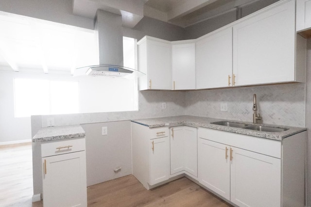 kitchen featuring light stone counters, light wood-style flooring, decorative backsplash, a sink, and wall chimney exhaust hood