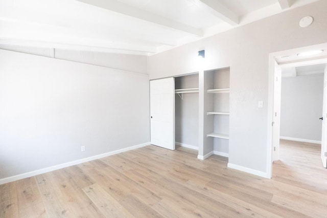 unfurnished bedroom with a closet, beam ceiling, baseboards, and wood finished floors