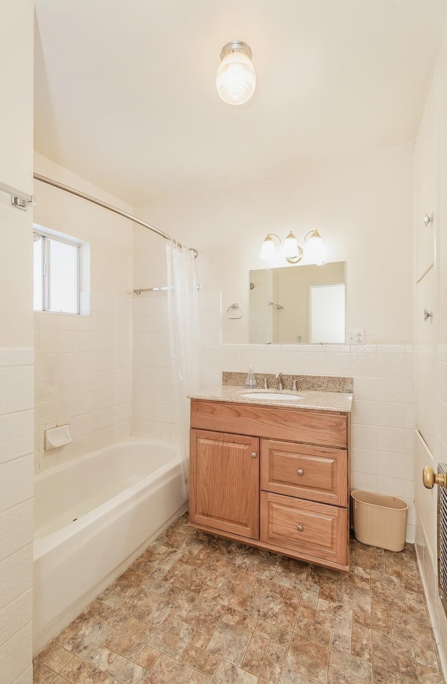 full bathroom with a wainscoted wall, tile walls, shower / bath combo, stone finish floor, and vanity