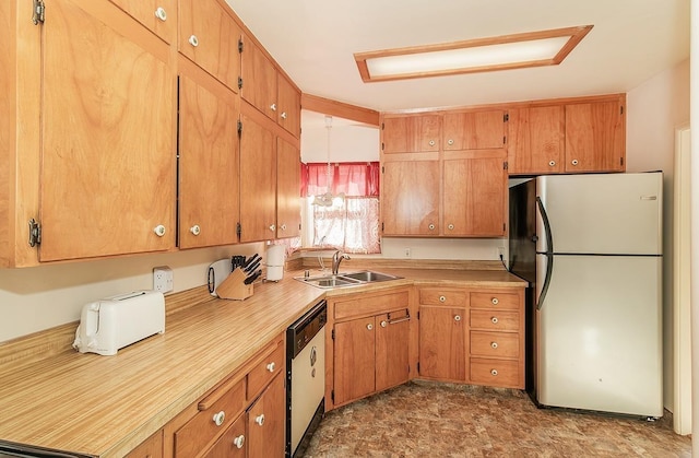 kitchen with dishwashing machine, a sink, light countertops, freestanding refrigerator, and brown cabinetry