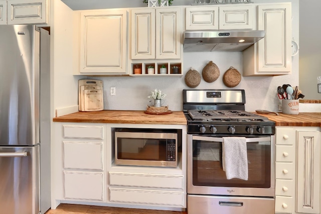 kitchen with appliances with stainless steel finishes, cream cabinetry, wooden counters, and under cabinet range hood