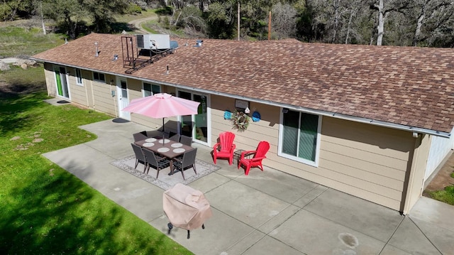rear view of house with central AC unit, a lawn, a shingled roof, and a patio