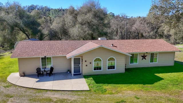 back of house featuring a patio area, a shingled roof, and a lawn