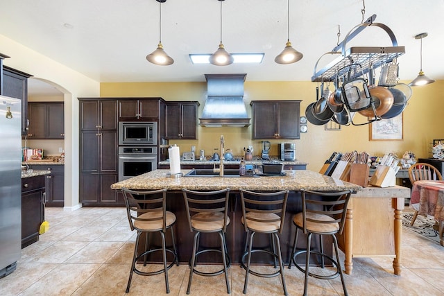 kitchen with stainless steel appliances, an island with sink, dark brown cabinetry, and custom range hood