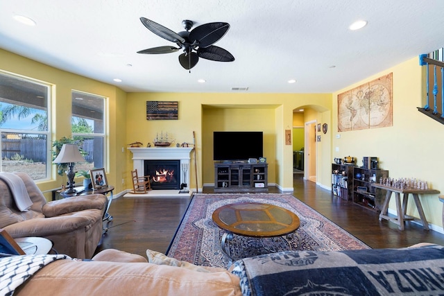 living area featuring visible vents, arched walkways, wood finished floors, and a lit fireplace