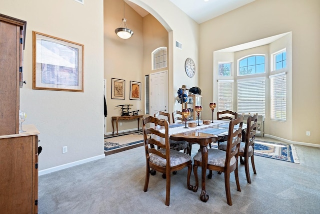 carpeted dining area featuring arched walkways, a high ceiling, visible vents, and baseboards