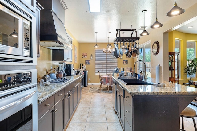 kitchen with light tile patterned floors, a breakfast bar area, a sink, appliances with stainless steel finishes, and custom exhaust hood