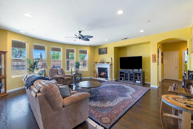 living room featuring a warm lit fireplace, wood finished floors, arched walkways, and visible vents