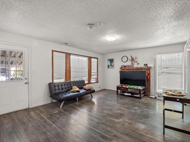 living room with a textured ceiling, wood finished floors, visible vents, and baseboards