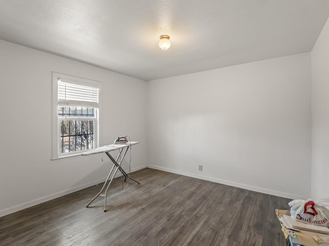 empty room featuring a textured ceiling, baseboards, and dark wood-type flooring